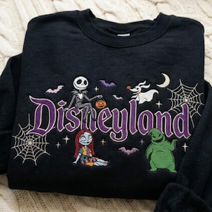 May include: A black crewneck sweatshirt featuring embroidered characters from The Nightmare Before Christmas. The word Disneyland is stitched in large purple letters, surrounded by Jack Skellington, Sally, Zero, Oogie Boogie, bats, and spiderwebs.