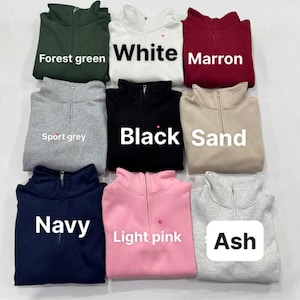 May include: A collection of nine quarter-zip sweatshirts in various colors, including forest green, white, maroon, sport grey, black, sand, navy, light pink, and ash. Each sweatshirt has a zipper and the color name is displayed on the front.