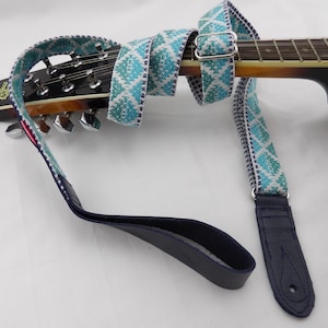 May include: A blue and white patterned guitar strap wrapped around a mandolin. The strap has a diamond pattern with a navy blue leather end and a silver buckle. The mandolin has a dark wood finish.