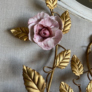 Puede incluir: Una decoraci&oacute;n de pared de metal dorado con una rosa de porcelana rosa y hojas doradas.