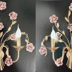 May include: Two gold wall sconces with a floral design featuring pink porcelain roses and white light bulbs. The sconces are made of metal and have a vintage style.