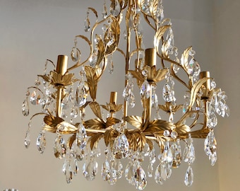 May include: A gold chandelier with crystal drops and leaf-shaped accents. The chandelier has a triangular shape and is suspended from a chain.