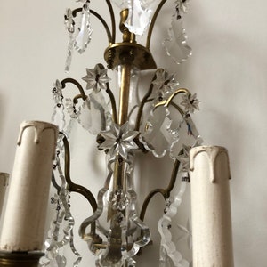 Peut inclure: Une applique murale en laiton et cristal au design traditionnel. L'applique poss&egrave;de cinq bougeoirs et pr&eacute;sente des gouttes et des &eacute;toiles en cristal complexes.