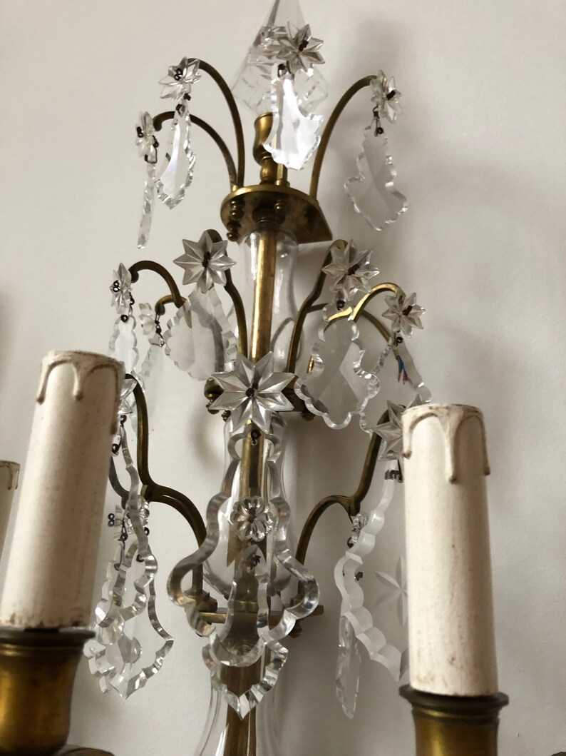 Peut inclure: Une applique murale en laiton et cristal au design traditionnel. L'applique poss&egrave;de cinq bougeoirs et pr&eacute;sente des gouttes et des &eacute;toiles en cristal complexes.