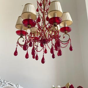 May include: A gold chandelier with red glass teardrop crystals and white fabric lampshades.
