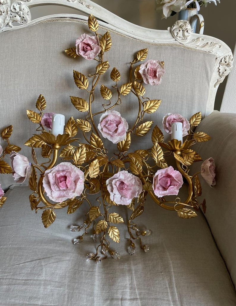 Puede incluir: Una l&aacute;mpara de pared de metal dorado con rosas de porcelana rosa y detalles de cristal. La l&aacute;mpara tiene un dise&ntilde;o floral con hojas y enredaderas.