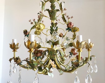 Puede incluir: Lámpara de araña ornamentada con un marco dorado, adornada con flores pintadas en tonos amarillos, rosas y marrones. La lámpara de araña presenta gotas de cristal transparente y accesorios de iluminación tipo vela, creando una lámpara elegante y decorativa.