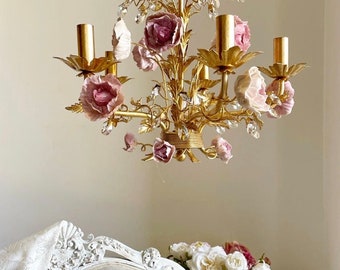 May include: A gold chandelier with pink porcelain roses and crystal accents. The chandelier has five arms and is decorated with leaves and vines.