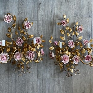 Puede incluir: Un par de apliques de pared doradas con rosas de porcelana rosa y detalles de cristal. Las apliques tienen forma de enredadera floral con hojas y flores.