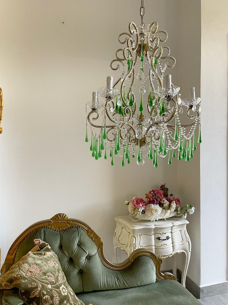 May include: A multi-armed chandelier featuring ornate gold-toned metal scrollwork, clear glass bobeches, and numerous dangling teardrop-shaped green glass crystals. The fixture is suspended by a chain and includes several light bulb sockets.