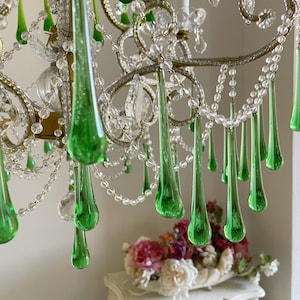 May include: A chandelier featuring numerous clear glass beads and elongated, teardrop-shaped green glass pendants. The fixture has a metallic frame with curved arms and clear crystal accents, creating a layered, hanging design with multiple light points.