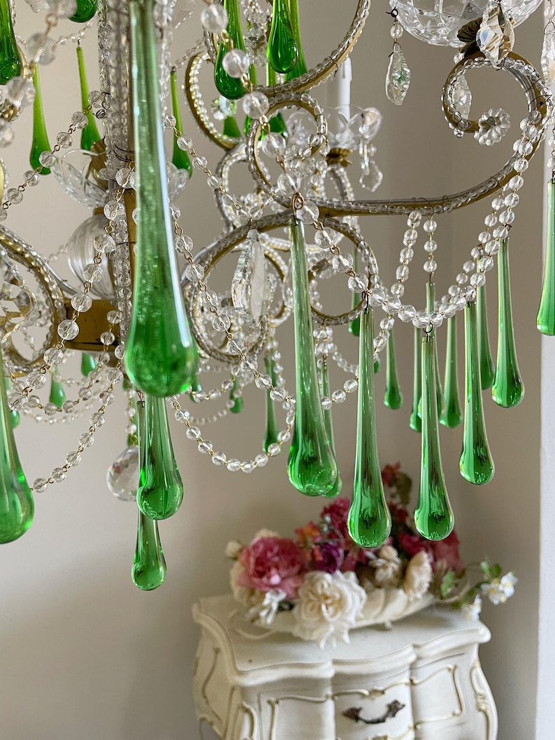 May include: A chandelier featuring numerous clear glass beads and elongated, teardrop-shaped green glass pendants. The fixture has a metallic frame with curved arms and clear crystal accents, creating a layered, hanging design with multiple light points.