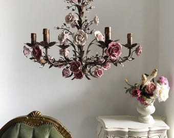 Puede incluir: Una lámpara de araña de varios brazos con una estructura de metal oscuro adornada con numerosas rosas de cerámica esculpida en varios tonos de rosa y blanco, intercaladas con pequeños cristales transparentes y cinco casquillos de vela.