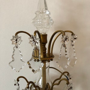 Peut inclure: Un lustre en laiton et en cristal avec une pointe en verre clair et plusieurs gouttes de cristal. Le lustre a un design traditionnel avec des d&eacute;tails orn&eacute;s.