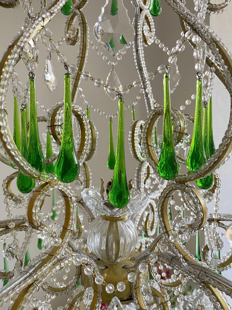 May include: A chandelier featuring a gold-toned metal frame adorned with numerous clear glass beads and vibrant green teardrop-shaped glass pendants. The structure includes curved metal arms, clear glass floral accents, and a central fluted glass base.