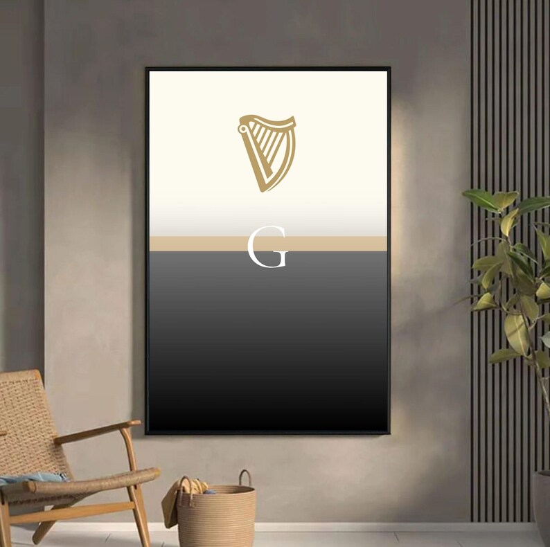 Guinness inspired “Split the G” framed poster styled in chic lounge with wicker chair and indoor plants, minimalist cream and black pint design with golden harp emblem, modern Irish wall art gift for Guinness fans, bold typography poster perfect for man caves, home bars, kitchens and pubs, sophisticated Guinness inspired décor, ideal artwork for beer enthusiasts, cultural Irish design with minimalist appeal in stylish home setting.
