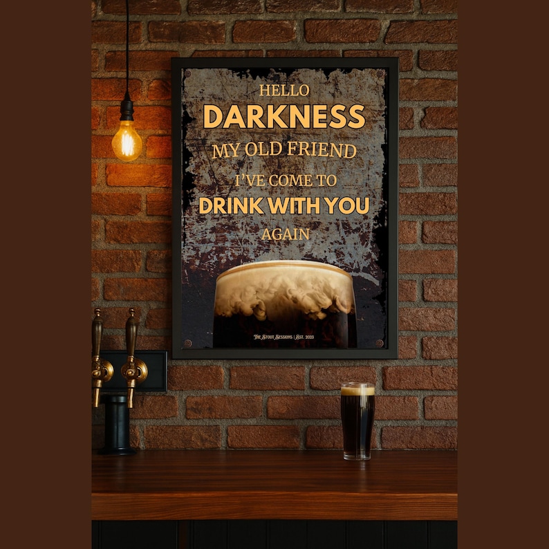 Guinness-inspired framed wall art poster styled against a warm-toned brick wall with vintage pendant lighting and a pint glass on a table below, creating a rustic home bar or speakeasy aesthetic.
