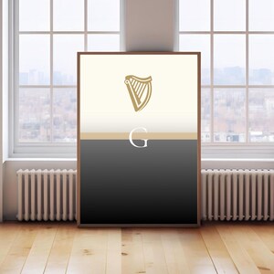 Guinness inspired “Split the G” poster leaning against large window interior, natural daylight reflecting on framed minimalist cream and black pint design, golden harp logo at top, bold Irish wall art, stylish Guinness fan décor, beer lover gift print, perfect for pubs, kitchens, man caves or living rooms, minimalist typography artwork celebrating Irish culture, sophisticated décor piece for modern interiors.