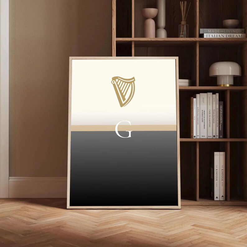 Guinness inspired “Split the G” minimalist poster framed and standing in modern wooden interior with shelving and décor elements, neutral tones highlighting the cream and black pint design, golden harp detail, stylish Irish wall art for homes, pubs, or beer lovers, ideal Guinness fan gift, bold typography artwork with cultural charm, versatile décor print suitable for contemporary or rustic spaces, highlighting Irish heritage and modern design.
