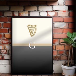 Guinness inspired “Split the G” framed wall art poster styled in industrial brick interior with natural greenery, minimalist cream and black pint inspired artwork with golden harp detail, bold Irish culture wall décor, perfect Guinness lover gift, contemporary print for modern homes, pubs, dining rooms, man caves or apartments, sleek Guinness inspired artwork, modern typography design, stylish and unique Irish heritage poster print.
