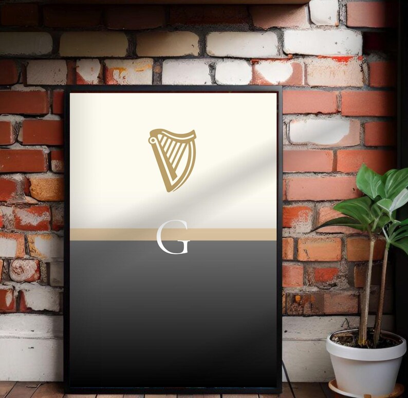 Guinness inspired “Split the G” framed wall art poster styled in industrial brick interior with natural greenery, minimalist cream and black pint inspired artwork with golden harp detail, bold Irish culture wall décor, perfect Guinness lover gift, contemporary print for modern homes, pubs, dining rooms, man caves or apartments, sleek Guinness inspired artwork, modern typography design, stylish and unique Irish heritage poster print.