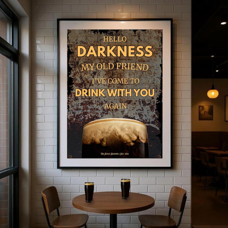 Hello Darkness My Old Friend I’ve Come to Drink With You Again” Guinness-inspired poster displayed in a stylish café interior, mounted on a white-tiled wall above a wooden table with two pint glasses, soft lighting, and warm industrial décor.
