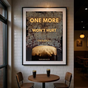 Framed One More Won’t Hurt Probably poster shown hanging above a small table in a pub style setting, featuring distressed textures, amber typography and stout inspired artwork, ideal wall art for home bars, kitchens, dining areas, pubs, offices and beer themed interiors with a dark humour aesthetic