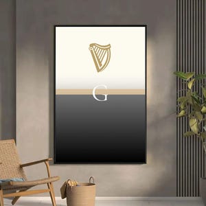 Guinness inspired “Split the G” framed poster styled in chic lounge with wicker chair and indoor plants, minimalist cream and black pint design with golden harp emblem, modern Irish wall art gift for Guinness fans, bold typography poster perfect for man caves, home bars, kitchens and pubs, sophisticated Guinness inspired décor, ideal artwork for beer enthusiasts, cultural Irish design with minimalist appeal in stylish home setting.