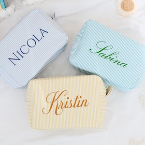 Puede incluir: Tres bolsas de cosméticos de tela a rayas con nombres personalizados: "Nicola", "Kristina" y "Salina".