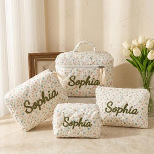 Puede incluir: Un conjunto de neceseres acolchados y un estuche de viaje con un estampado floral en blanco, azul y rojo. Cada pieza está bordada con el nombre "Sophia" en verde. El conjunto incluye una bolsa cuadrada pequeña, una bolsa rectangular, una bolsa rectangular más grande y un estuche de viaje con asa.