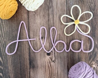May include: A purple string art name sign that says "Alba" with a white daisy flower with a yellow center.