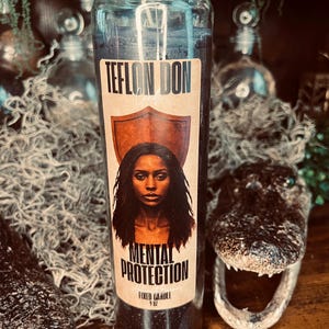 Puede incluir: Una vela de cristal cilíndrica y alta rellena de cera negra. La etiqueta presenta el texto "TEFLON DON", "MENTAL PROTECTION" y "FIXED CANDLE 9 OZ" junto a la ilustración de una persona con pelo largo y oscuro frente a un escudo.