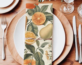 Puede incluir: Una servilleta de lino blanca con un estampado de cítricos. La servilleta presenta naranjas, limones y hojas en tonos verdes, amarillos y naranjas. La servilleta está doblada y colocada sobre una mesa de madera.