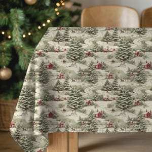 Könnte beinhalten: Eine cremefarbene Tischdecke mit einer Winterszene mit immergrünen Bäumen, roten Häusern und kurvenreichen Straßen. Das Design wiederholt sich über den Stoff und schafft ein festliches Urlaubsthema. Die Tischdecke ist über einem Holztisch drapiert.