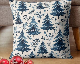 Könnte beinhalten: Quadratisches Kissen mit cremefarbenem Hintergrund und einem sich wiederholenden Muster aus blauen Aquarell-Weihnachtsbäumen und Zweigen. Rote und goldene Weihnachtskugeln sind im Vordergrund.