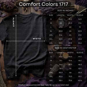 Puede incluir: Camiseta negra Comfort Colors 1717 con tabla de tallas en centímetros. La tabla muestra las medidas de largo, ancho y manga para las tallas S a 4XL. Las medidas de la camiseta varían hasta 3,8 cm.