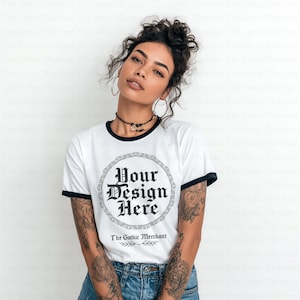 Puede incluir: Camiseta blanca con cuello redondo y ribete negro con el texto "Your Design Here" en fuente gótica. La camiseta forma parte de una línea de ropa y está hecha de un material suave. También es visible el logotipo de The Gothic Merchant.