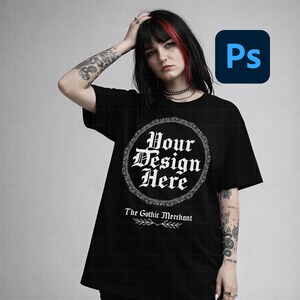May include: Black t-shirt with a round white design that says "Your Design Here" in a gothic font. The text "The Gothic Merchant" is below the design. The shirt is worn by a person with tattoos and red highlights in their hair.