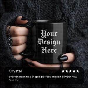 May include: Black ceramic mug with the text "Your Design Here" in white gothic font. The mug is held by a person with black nail polish and rings. The mug is a standard size for coffee or tea.