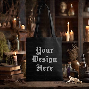 May include: Black tote bag with the text "Your Design Here" in a gothic font. The bag has long handles and is displayed on a wooden surface. The background includes candles, books, and apothecary bottles.