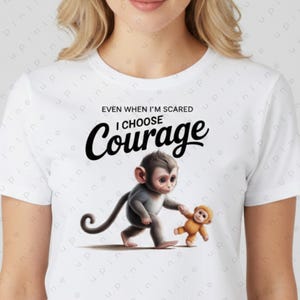 May include: White t-shirt with a graphic of two cartoon monkeys. A grey monkey is holding the hand of a smaller, orange monkey. The text "EVEN WHEN I'M SCARED I CHOOSE Courage" is above the monkeys.