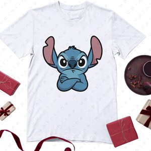 May include: White t-shirt featuring a cartoon illustration of Stitch from Lilo & Stitch. The blue character has crossed arms and an angry expression. The shirt is surrounded by wrapped gifts and a decorative plate.