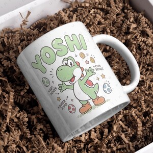 May include: White ceramic mug featuring the character Yoshi from the Super Mario video game series. The mug has a green Yoshi graphic with the word "YOSHI" in green bubble letters. Additional graphics include coins, eggs, and the phrases "Egg Power" and "Super Jump."