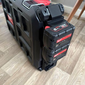 May include: Black and red Milwaukee tool storage system with attached battery packs. The system is made of durable plastic and features multiple compartments. The battery packs are labelled "REDLITHIUM M18 5.0 Ah".
