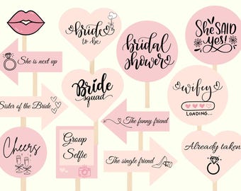 Puede incluir: Una colección de accesorios rosas para fotomatón para una despedida de soltera. Los accesorios incluyen letreros con frases como "Bride to be", "She said yes" y "Bride squad". Otros accesorios incluyen labios, flechas y corazones.