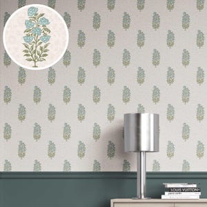 Op de afbeelding: Behang met een herhalend patroon van blauwe bloemmotieven op een crèmekleurige achtergrond. Het ontwerp omvat groene stelen en bladeren. Een close-up toont het bloemmotief. Een zilveren lamp en boeken staan op een witte kast.