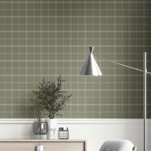 May include: Olive green plaid wallpaper with a white grid pattern. A modern silver lamp with a cone-shaped shade is positioned to the right. A white trim runs along the bottom, with a wooden cabinet and decorative items.