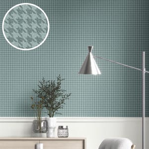 May include: A teal and gray houndstooth pattern covers the wall, with a close-up in a circle showing the detail. A silver lamp and a small plant sit in front of the wall. A white trim and a wooden cabinet are also visible.