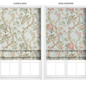 May include: Two Roman shades with floral and bird patterns. The left shade, labeled "Cuddle Bug," features a light blue background with brown branches, green leaves, and blue birds. The right shade, labeled "Ring Whisper," has a similar design with pink flowers.