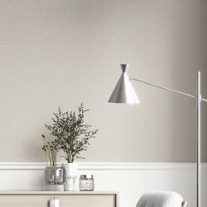 May include: A neutral-toned room with a textured wallpaper background. A silver floor lamp with a conical shade is positioned to the right. A wooden cabinet holds decorative vases and a small glass jar. The room has a minimalist, modern aesthetic.